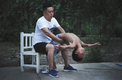 刘甫正在帮助一位小男孩儿练习下腰.